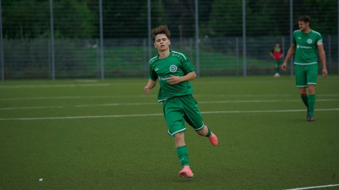 A football player in a green jersey running during an outdoor match on a grass pitch.