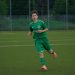 A football player in a green jersey running during an outdoor match on a grass pitch.